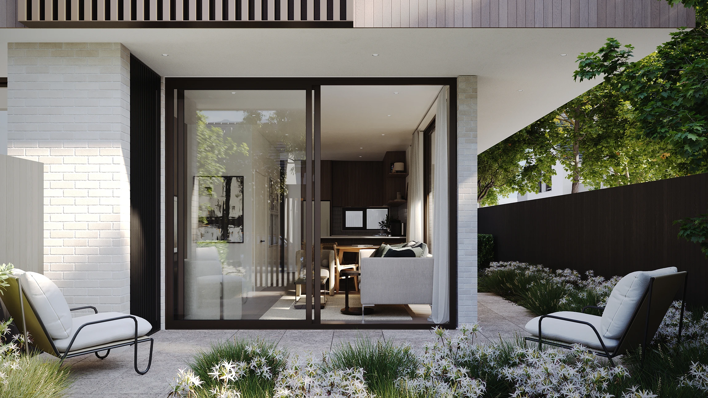 Modern courtyard living room with sliding glass doors, two cushioned outdoor chairs, greenery, and white flowering plants.
