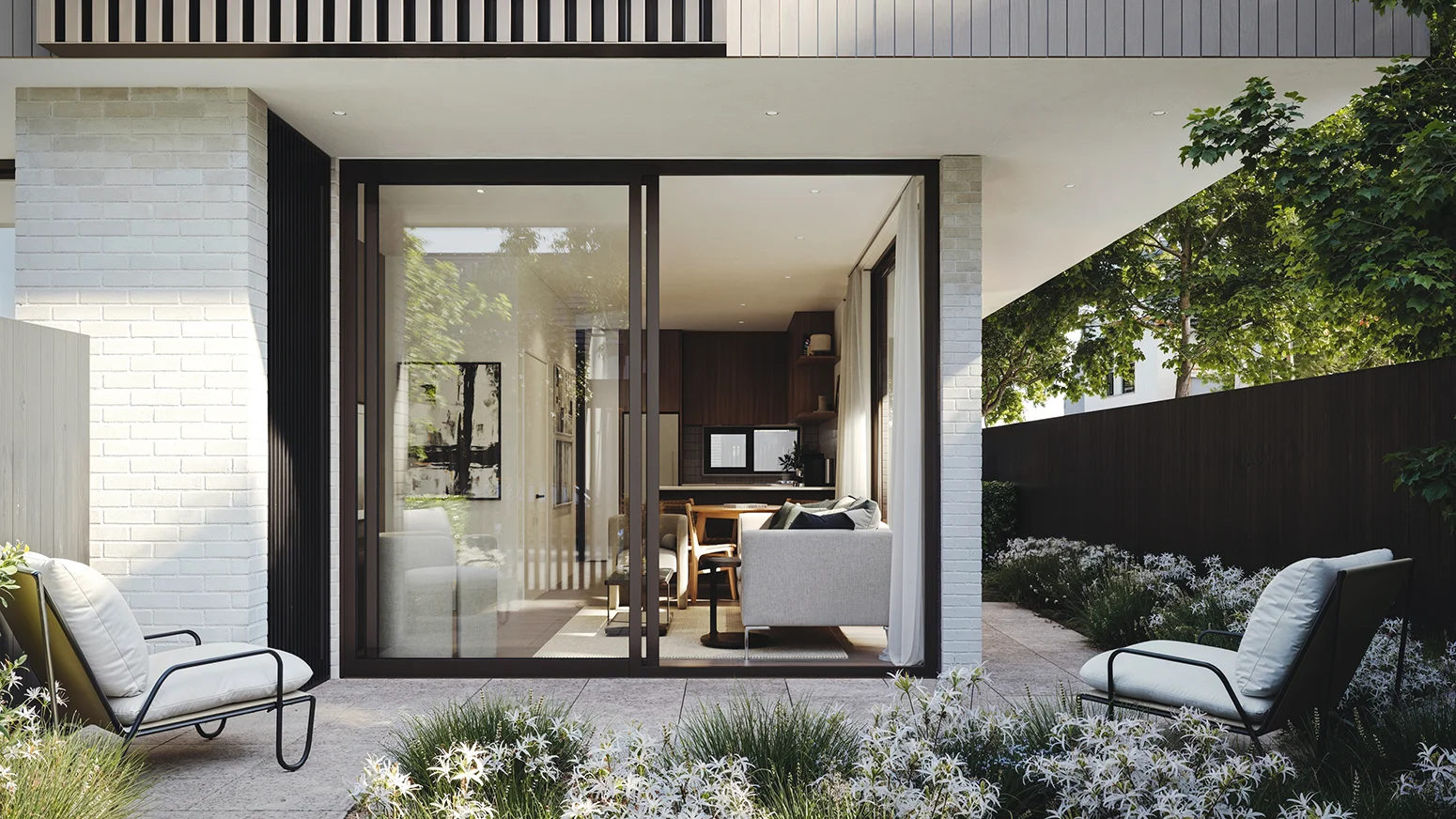 Modern house courtyard with two cushioned chairs, flowering plants, and a glass sliding door to living room.