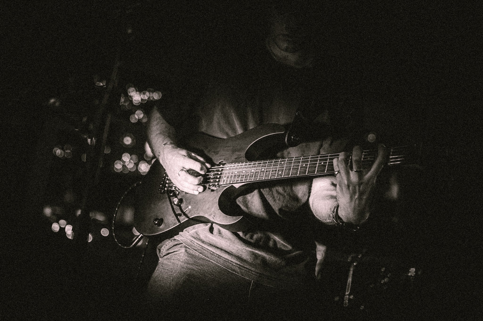 Black and white close-up of a person from REDACTED playing an electric guitar in low light