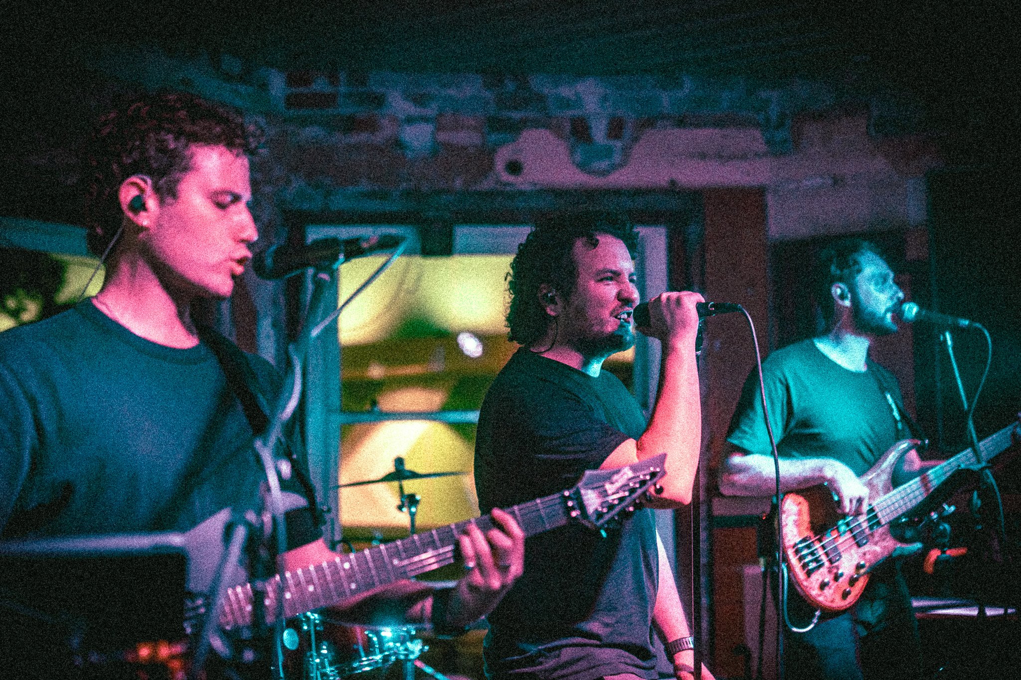 Three musicians from REDACTED performing live on stage, with one singing into a microphone, one playing guitar, and one playing bass guitar.