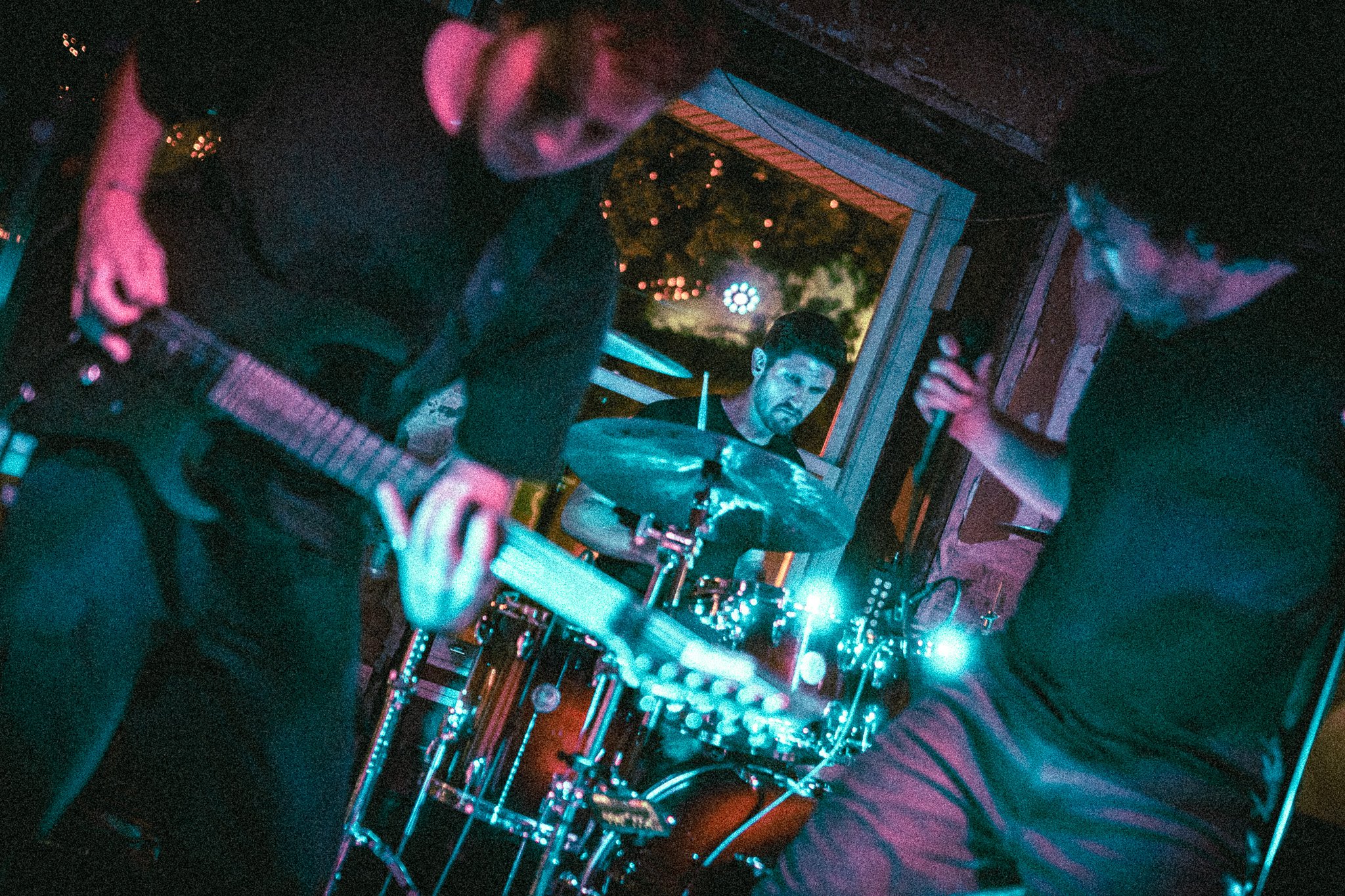 REACTED Band performing live with a guitarist, drummer, and singer illuminated by blue and pink stage lights.