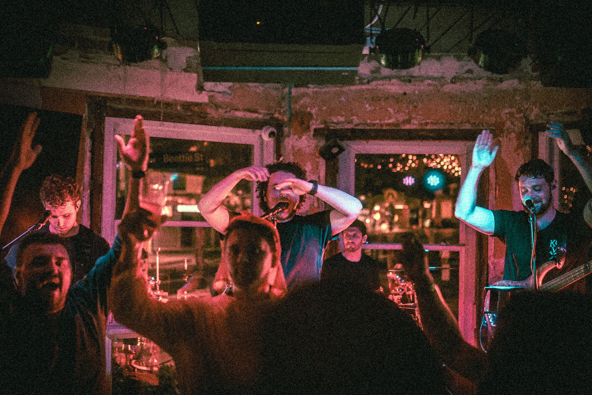 REDACTED Band performing live indoors with audience raising hands and colorful stage lights.