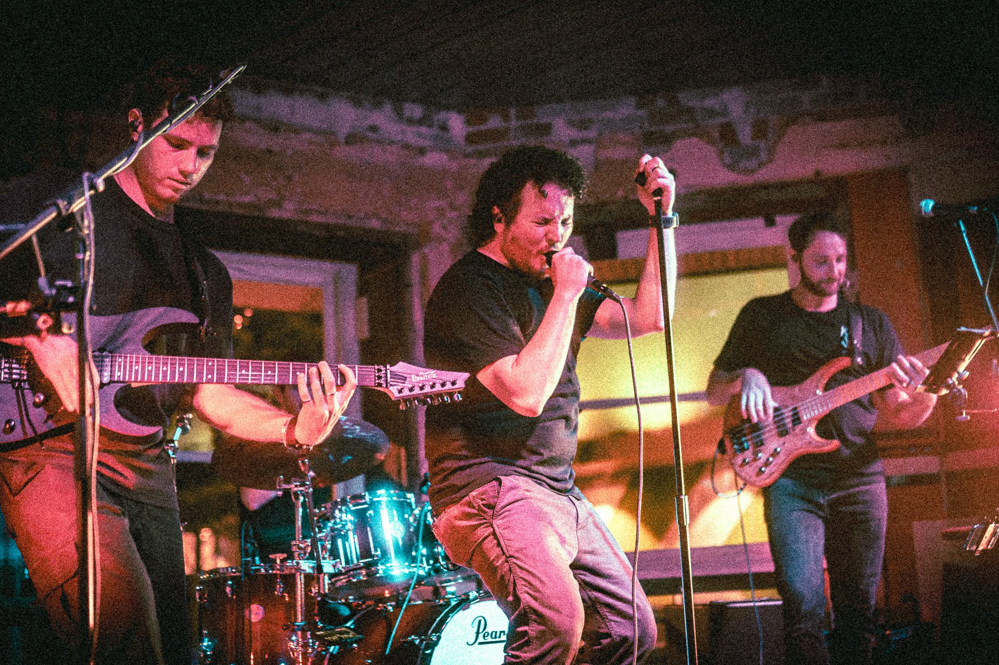 REACTED band performing live with two guitarists, a singer with a microphone, and a drummer in the background.