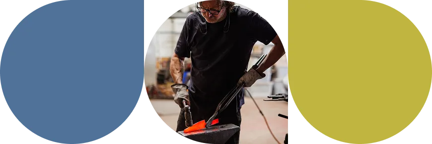 Blacksmith wearing gloves using tongs to shape a glowing hot piece of metal on an anvil in a workshop.
