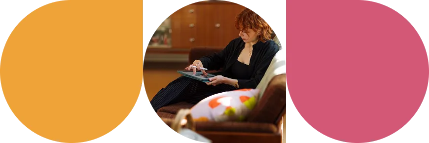 Woman with red hair sitting on a brown sofa, using a tablet with a stylus pen.