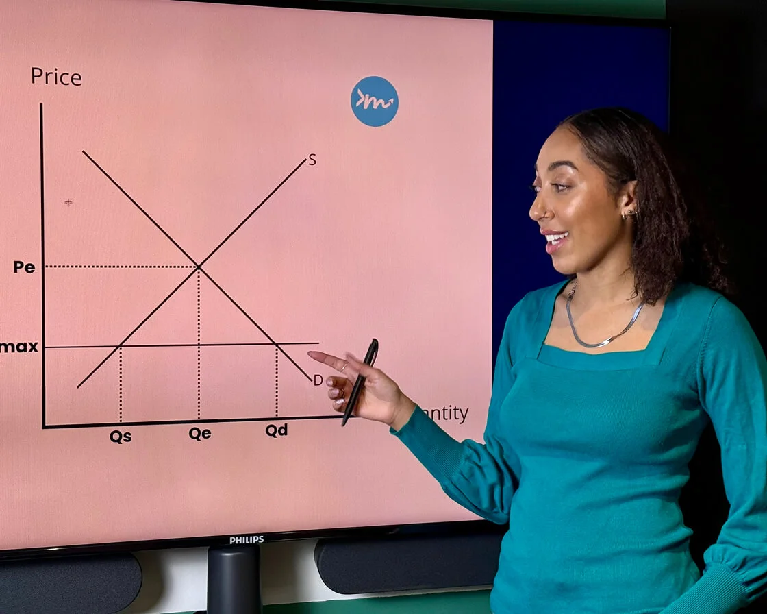 Asha Wadley is tutoring economics online, standing before a large screen displaying a graph.