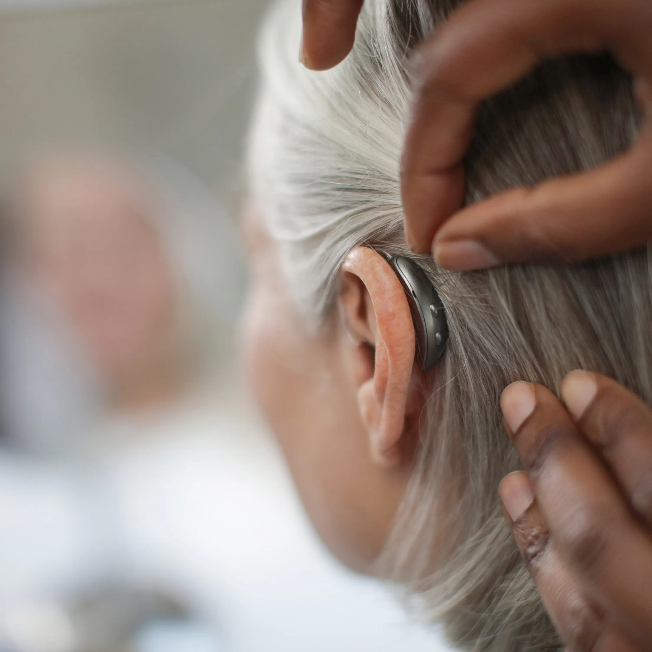 Close-up of a person adjusting a hearing aid behind their ear with grey hair visible.