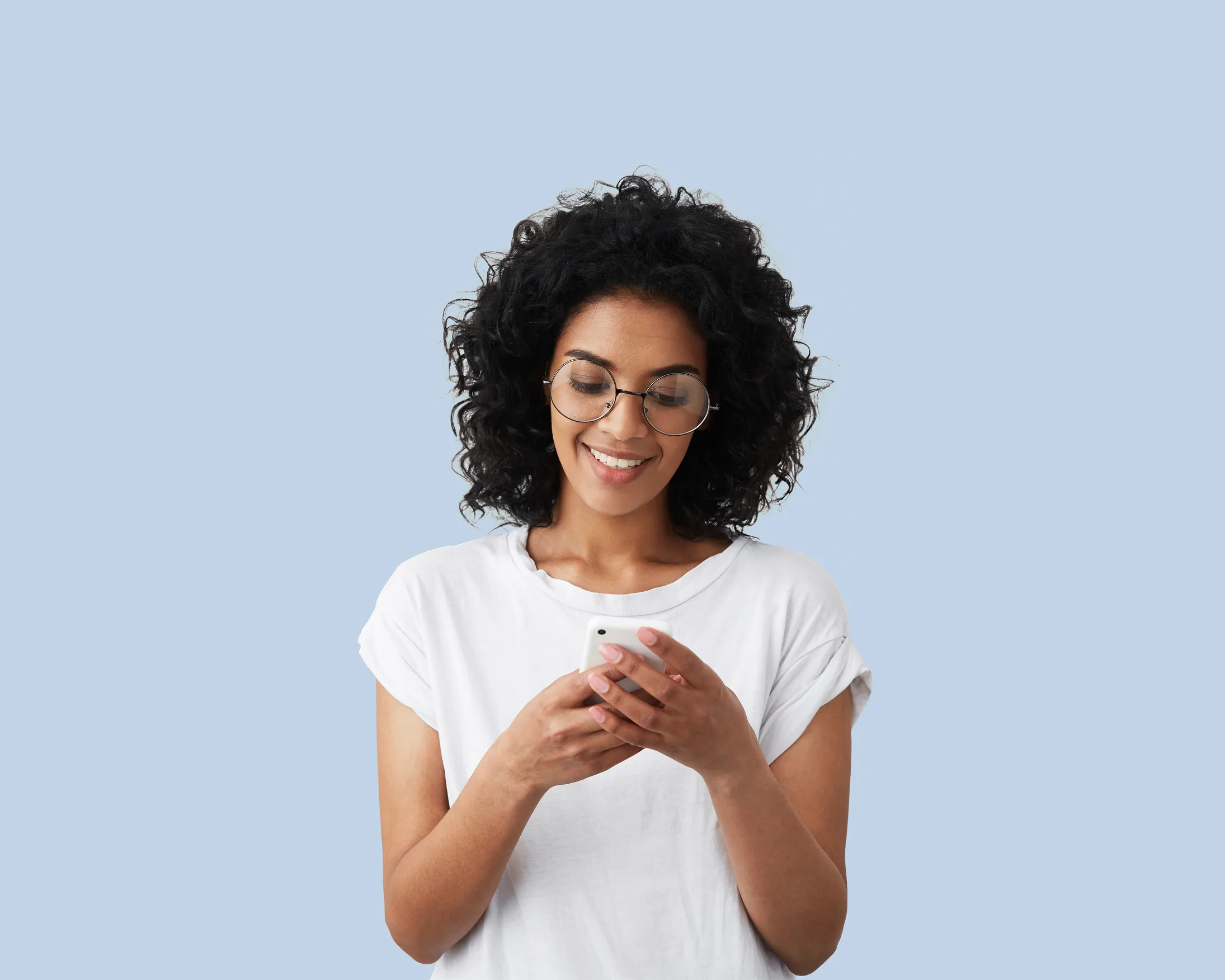Smiling woman with curly hair and glasses looking at her smartphone against a light blue background.