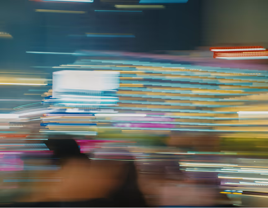 Blurred cityscape at night with streaks of colorful lights and indistinct shapes suggesting movement.
