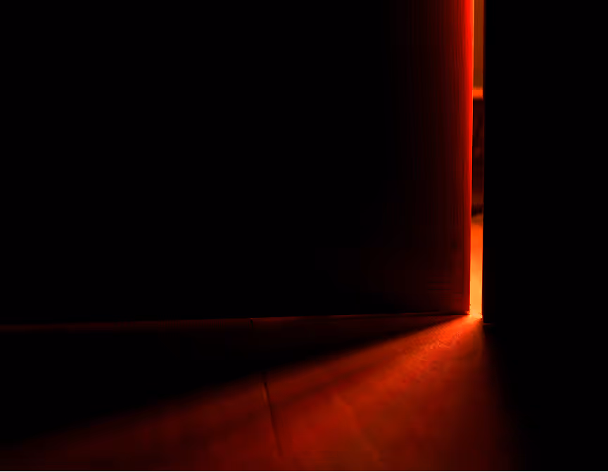 Narrow gap of a door slightly open with red light streaming through onto the floor in a dark room.