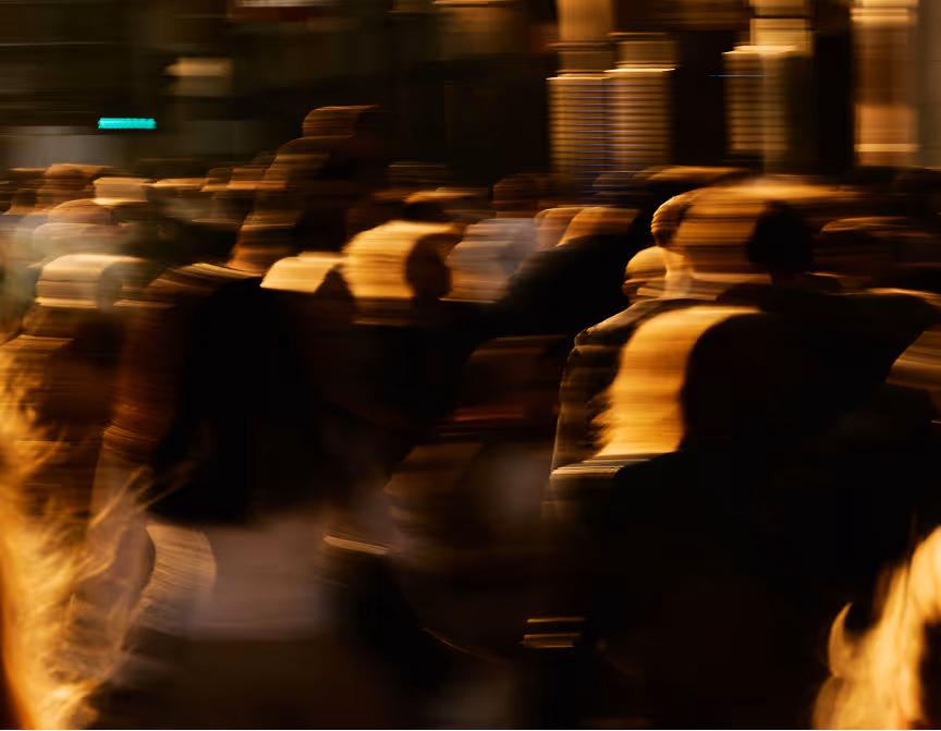 Blurred crowd of people walking in an urban setting with warm lighting.