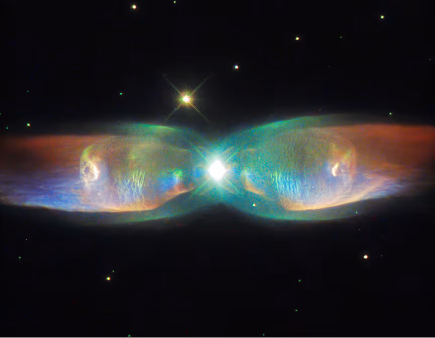 Bright star at center with colorful, symmetrical, translucent nebula clouds extending horizontally in space with smaller stars in the background.