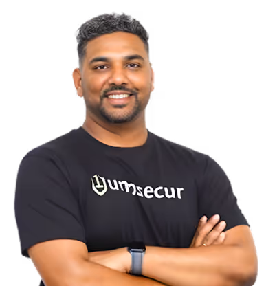 Smiling man with short hair and beard wearing a black Tumsecur t-shirt and a smartwatch, arms crossed.
