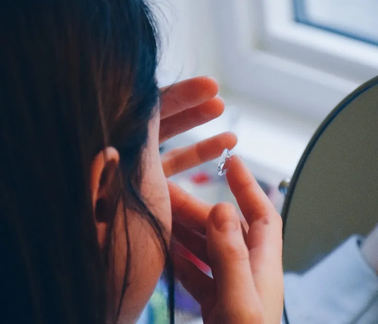 Close-up of a person holding a contact lens on their fingertip in front of a mirror.