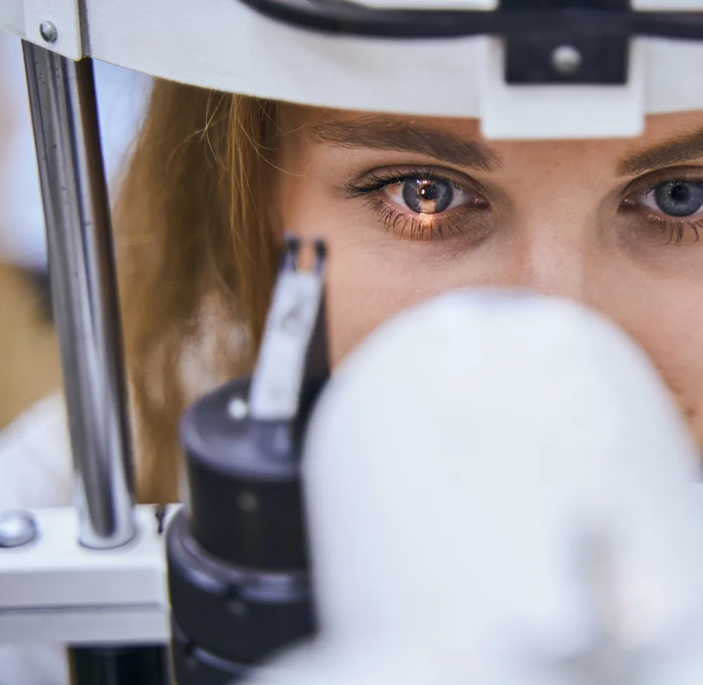 Close-up of a woman undergoing an eye examination looking into an ophthalmic device.