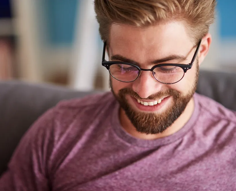 Smiling bearded man with glasses wearing a purple shirt, looking down.