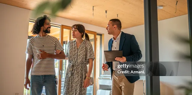 Three people having a discussion indoors, with one man holding a tablet and two others listening.