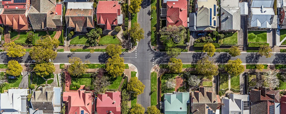 Aerial view of a suburban neighborhood intersection with houses, lawns, trees, and streets.