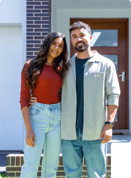 Smiling couple standing outside a house entrance, the man has his arm around the woman.