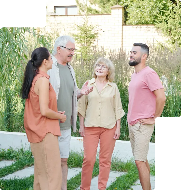 Two older adults and two younger adults standing outside in a garden, engaged in conversation and smiling.