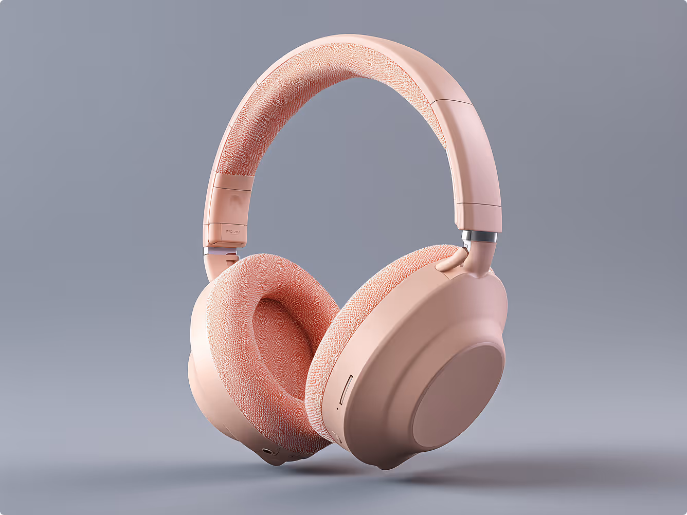 Minimalist over-ear wireless headphones in a soft pink finish, shown floating against a neutral background with fabric ear cushions.