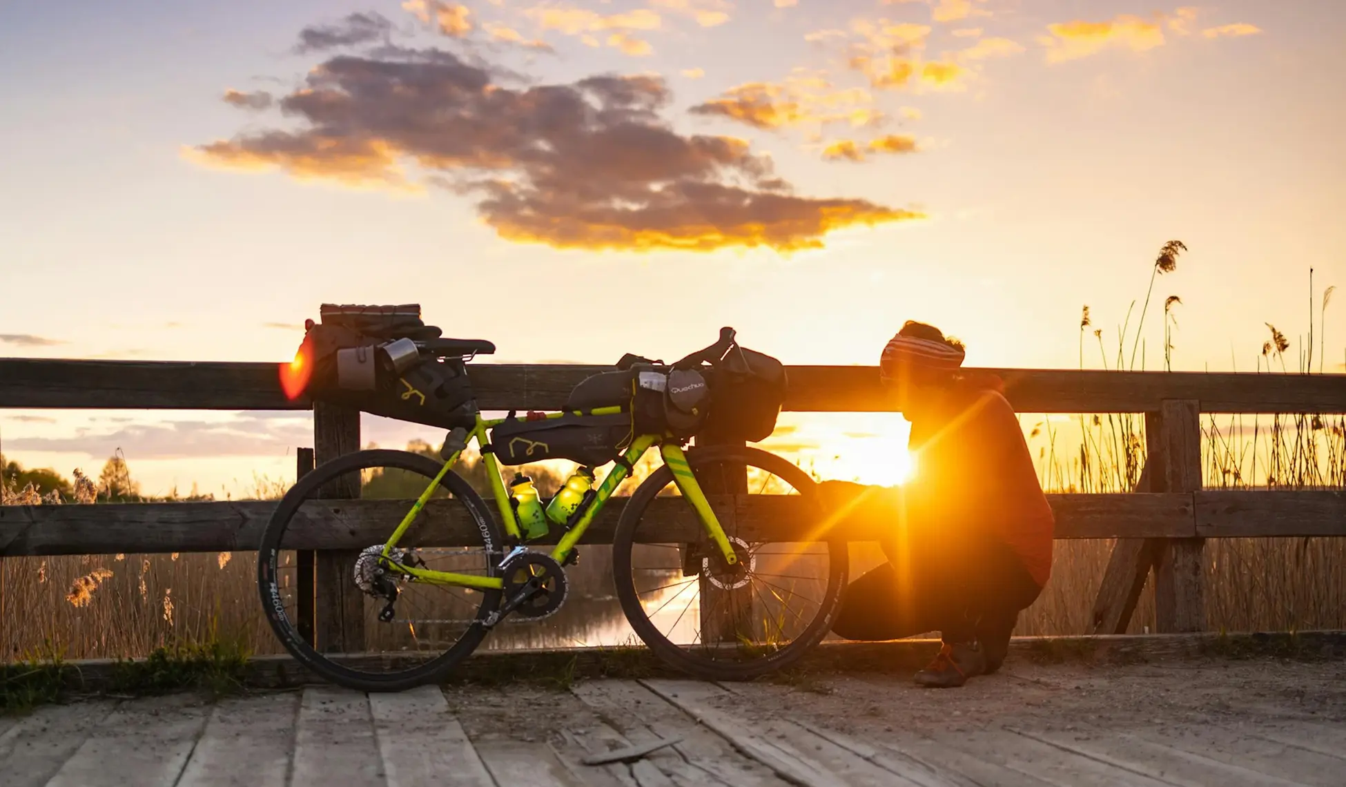 Bicycle loaded with gear resting on a wooden bridge at sunset, symbolizing endurance, travel, and mental resilience.