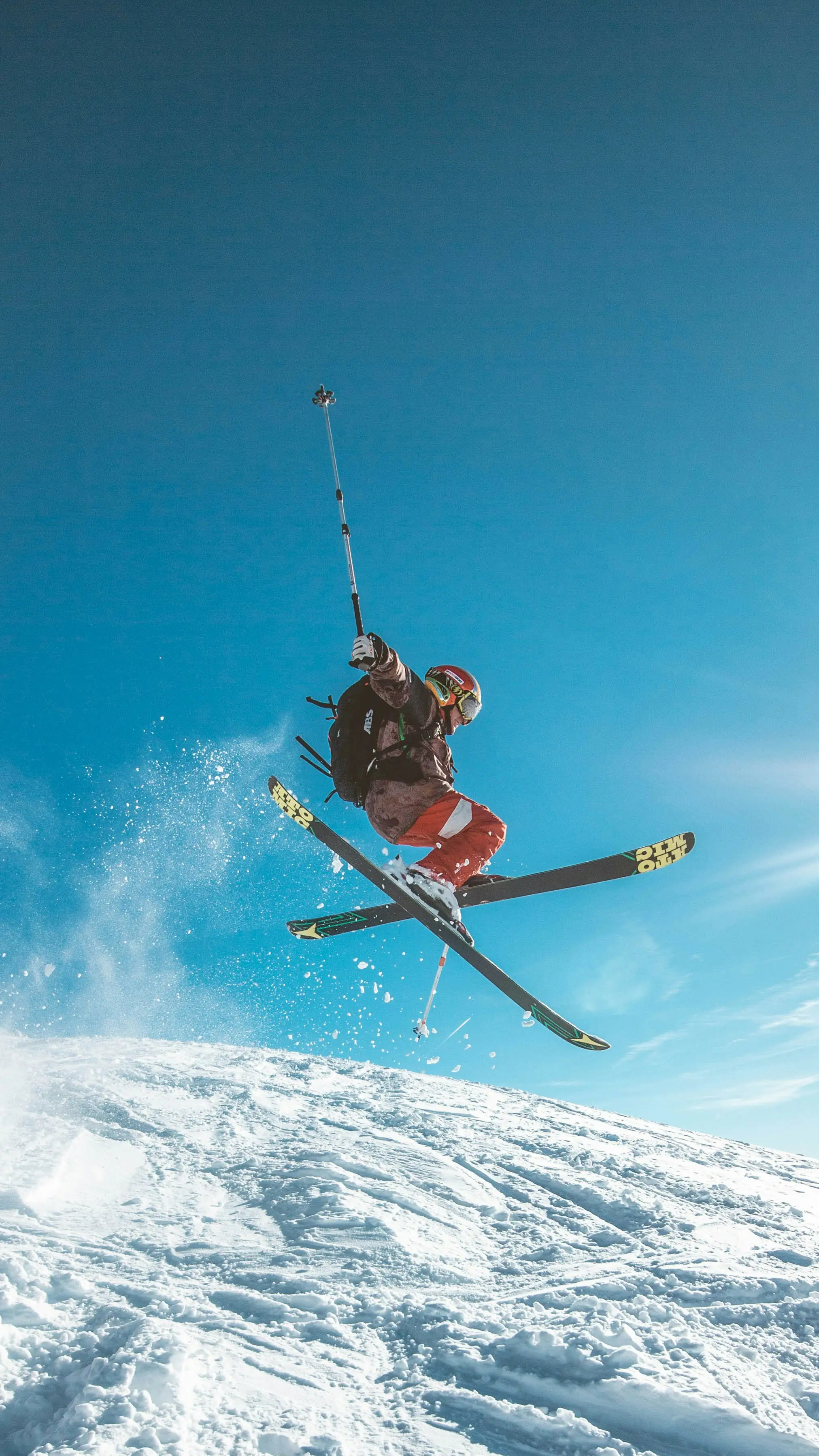 Noah Carter sky skiing high above a mountain landscape, suspended in the air with skis on and a parachute overhead.