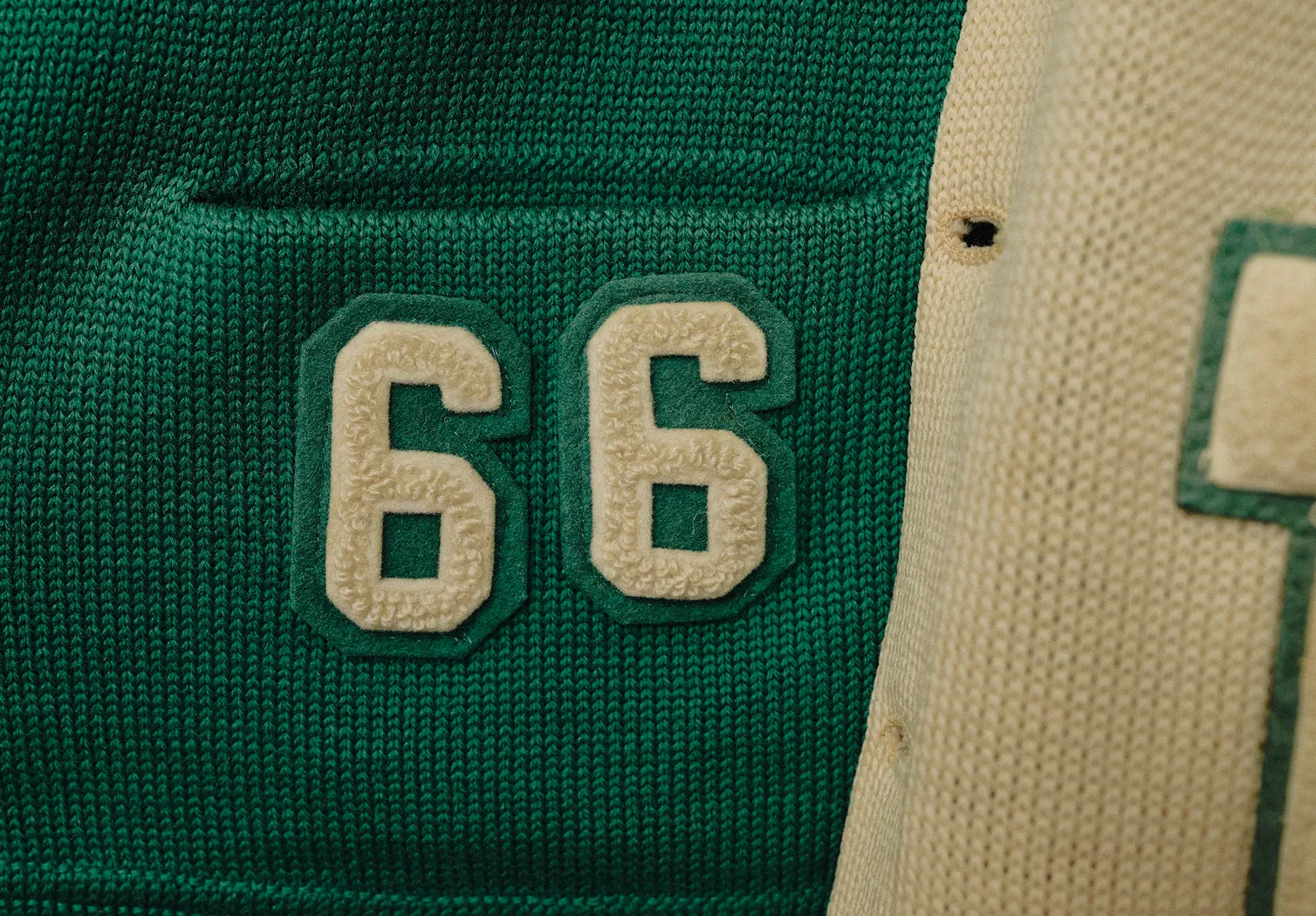 Green knitted fabric patch with cream-colored textured number 66 on a cream knit background.