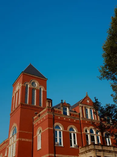 Red brick historic building with arched windows and a tower against a clear blue sky.