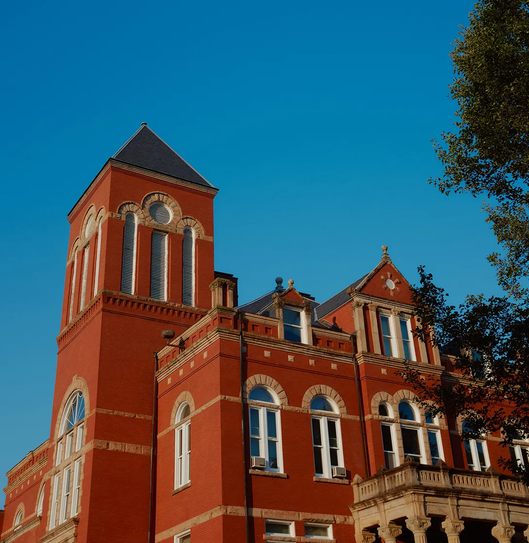Red brick historic building with arched windows and a tall clock tower under a clear blue sky.