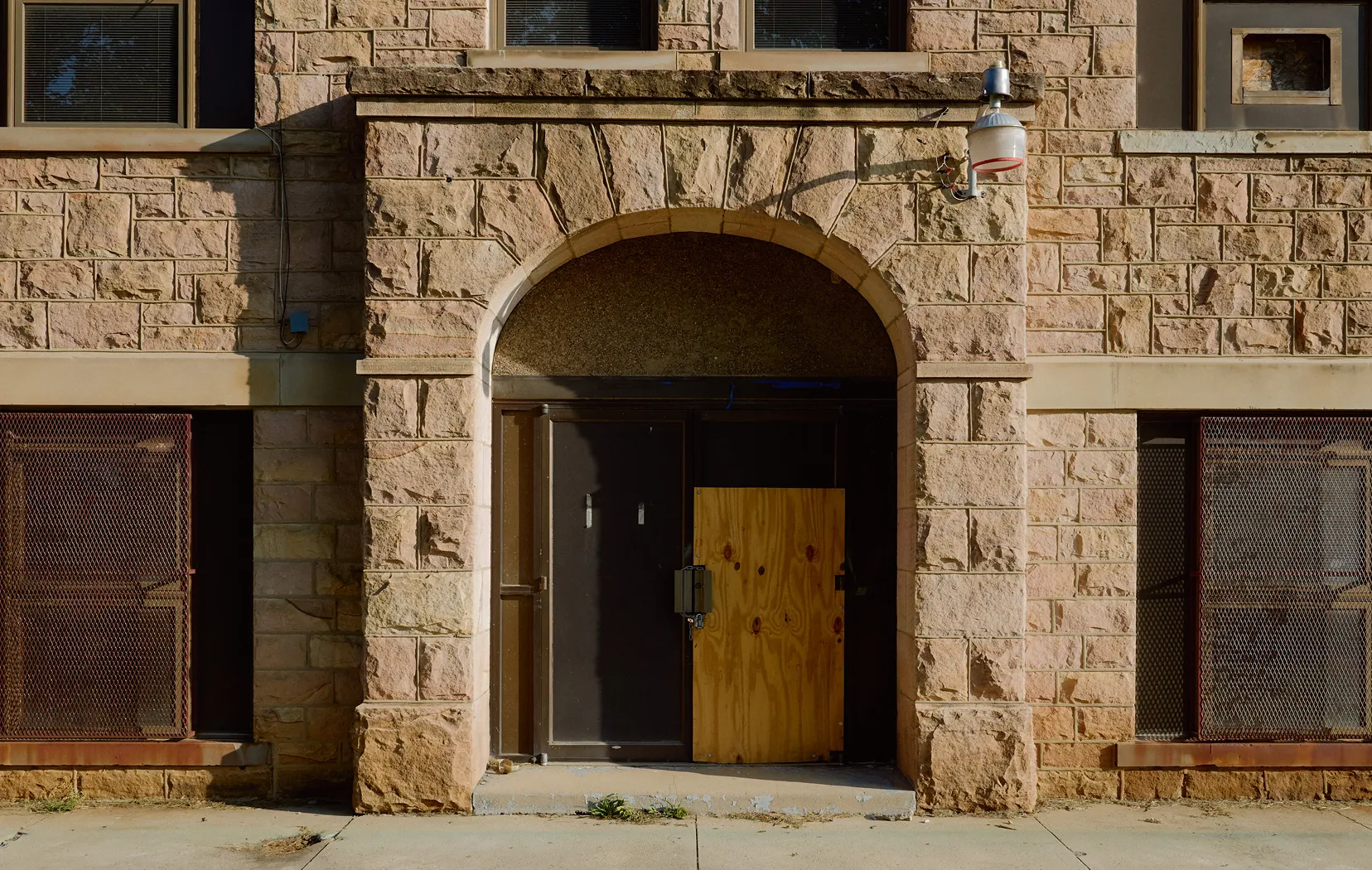 Stone building facade with an arched entrance and a partially boarded-up dark doorway.