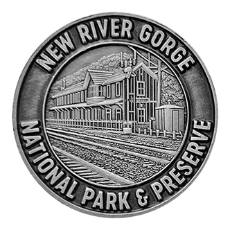 Metal emblem showing a historic train station with railroad tracks, labeled New River Gorge National Park & Preserve.