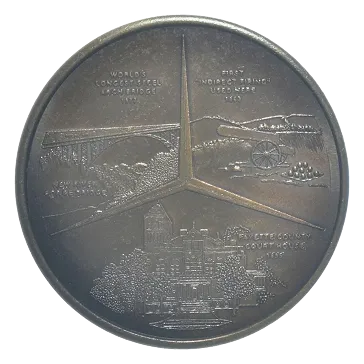 Round commemorative medal divided into three sections illustrating the world's longest steel railway bridge from 1910, the first indigenous artillery used in 1855, and a government building established in 1911.