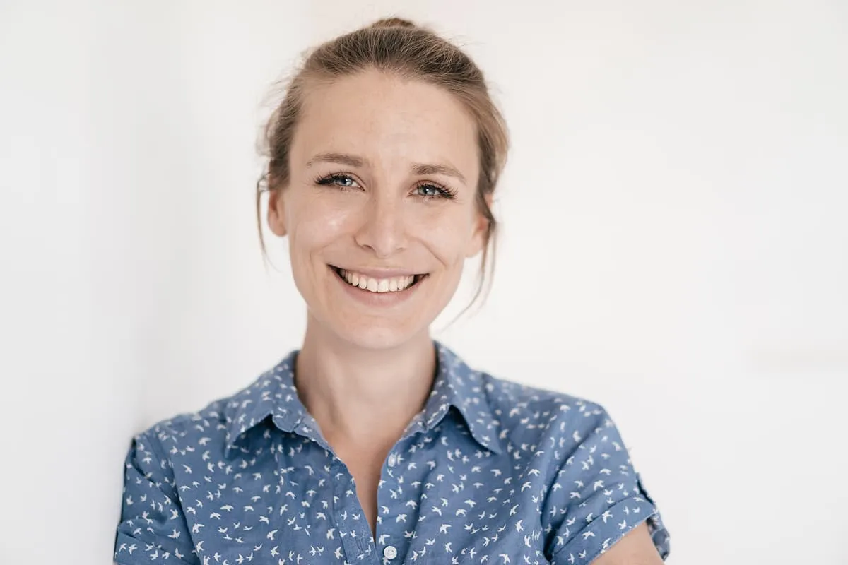 Smiling woman with blue eyes and light brown hair tied back wearing a blue shirt with small white bird patterns.