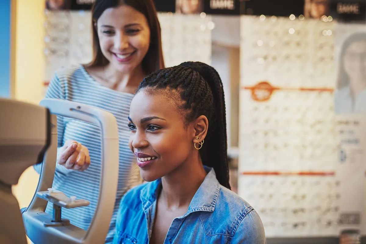 Smiling woman with braided hair undergoing an eye examination with an optometrist in an optical store.