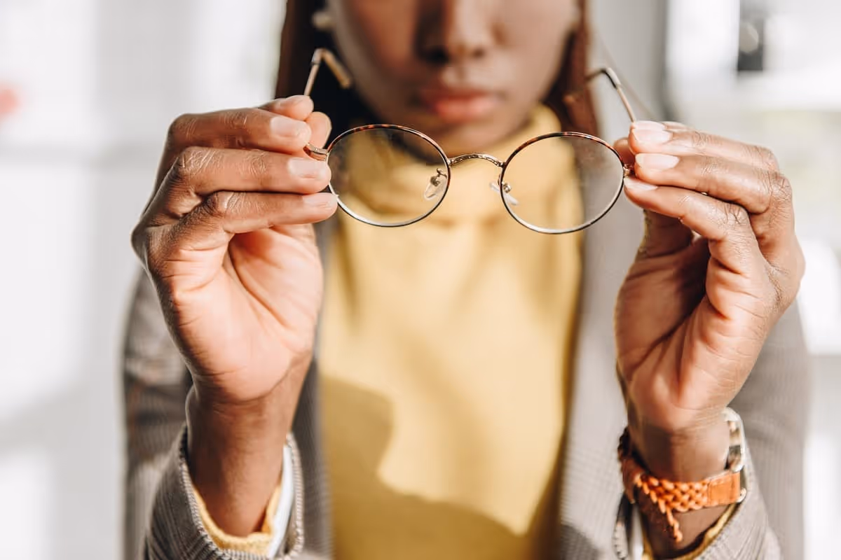 Person holding a pair of round eyeglasses in both hands with a blurred background.