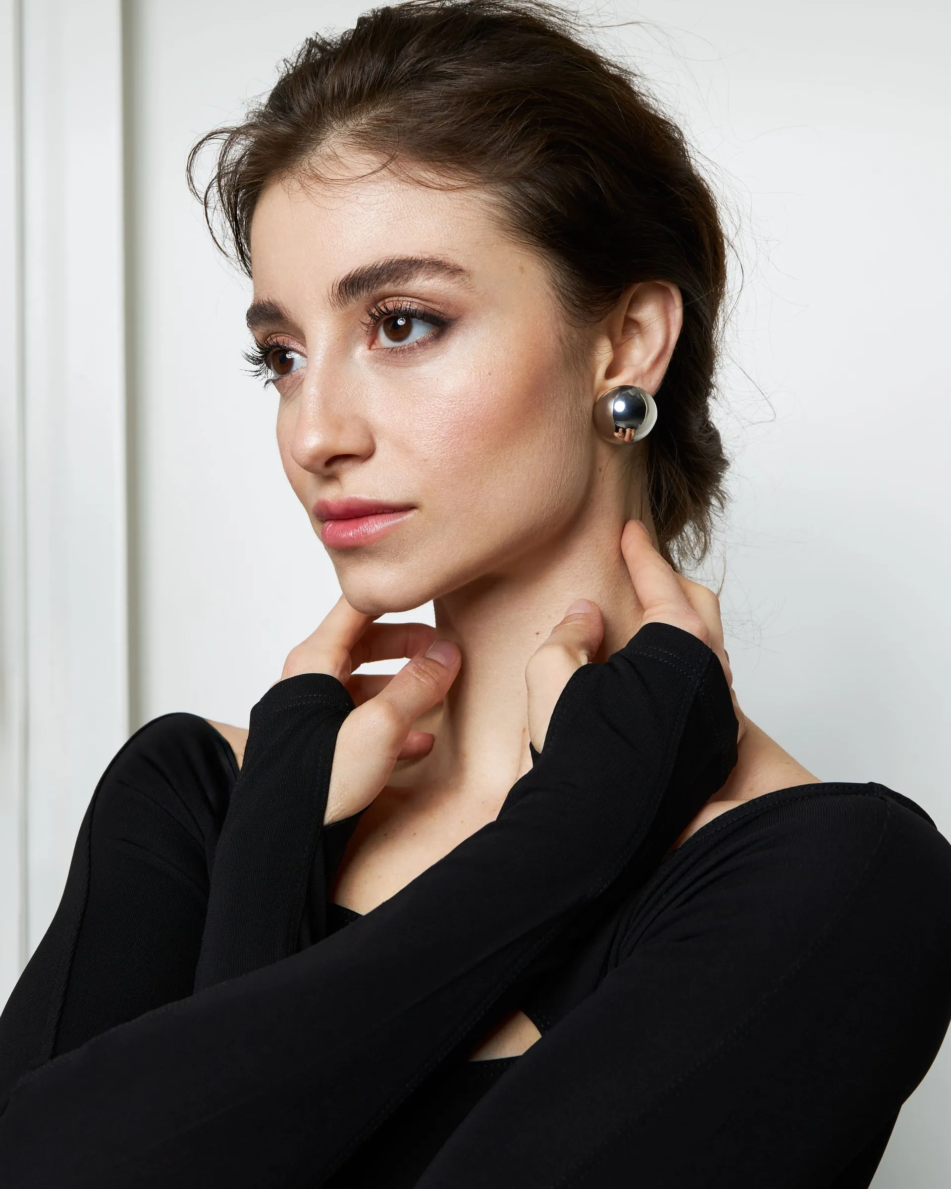 Woman with dark hair, wearing a black top and silver earrings, touching her neck