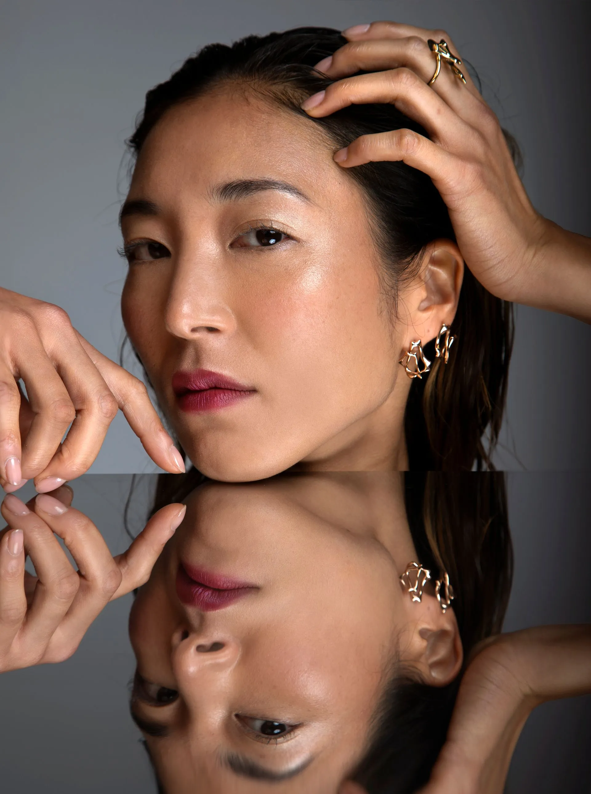 Woman with wet hair, hands touching head and reflection. Dark lipstick, gold earrings, studio setting