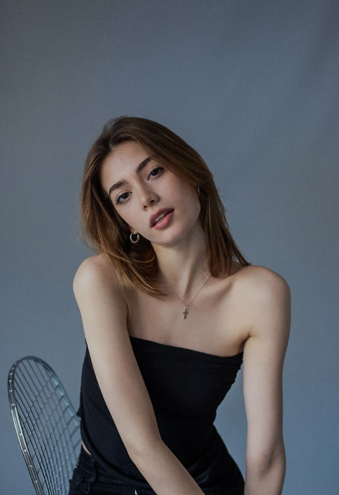 Woman in black tube top, sitting, looking at the camera, neutral background