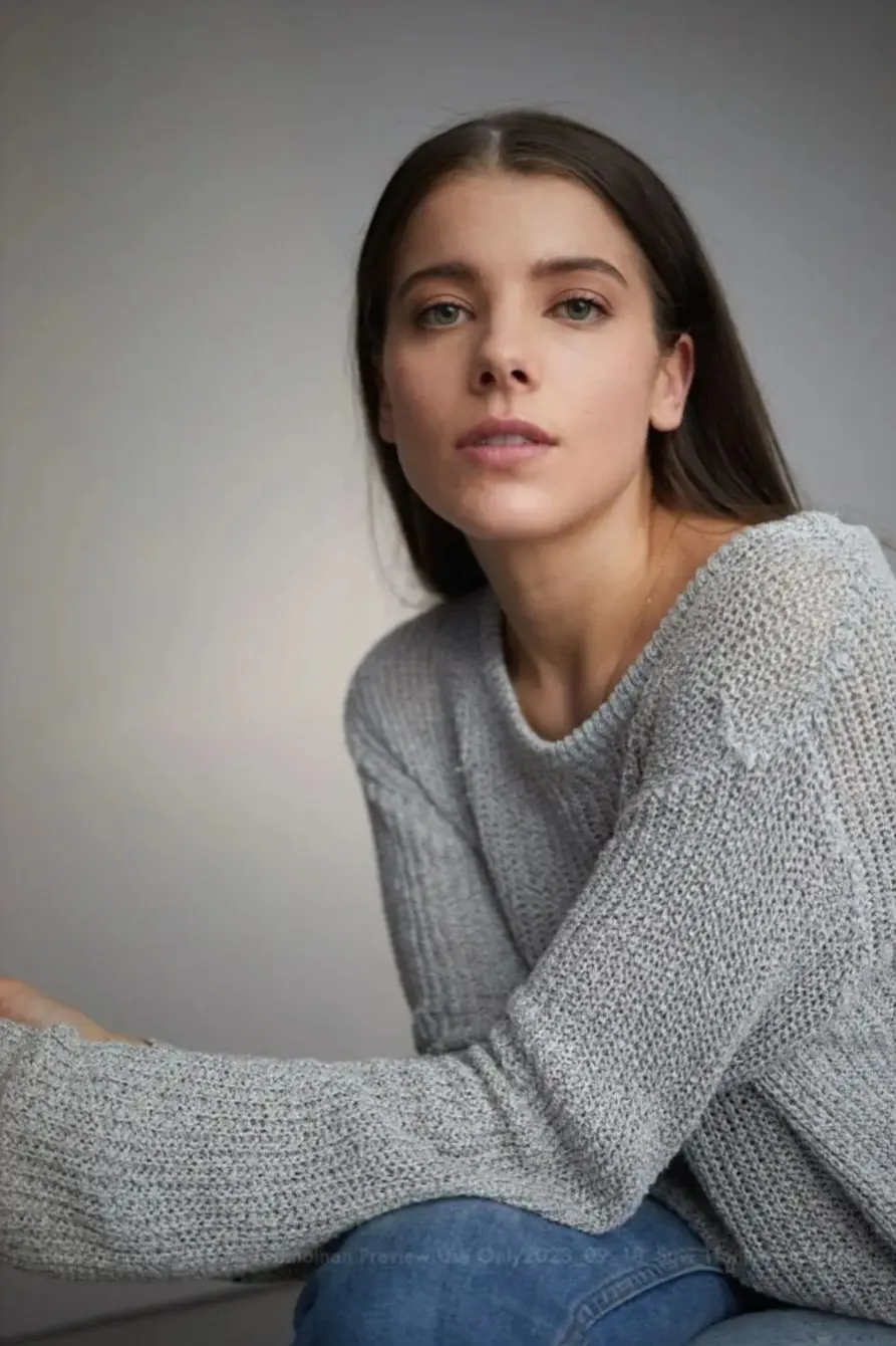 Woman in a gray sweater and blue jeans, looking at the camera