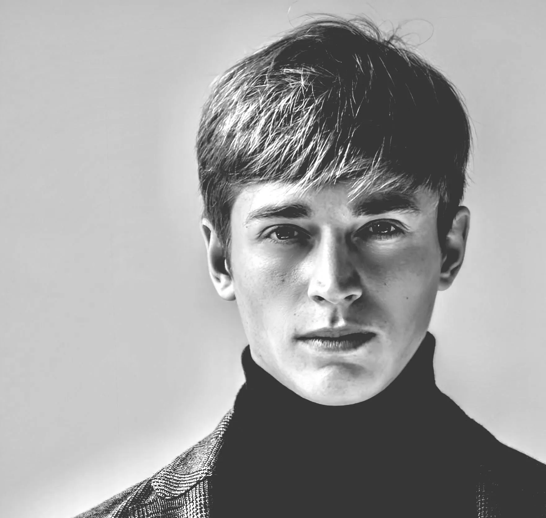 Man wearing a black turtleneck and patterned jacket, looking at the camera