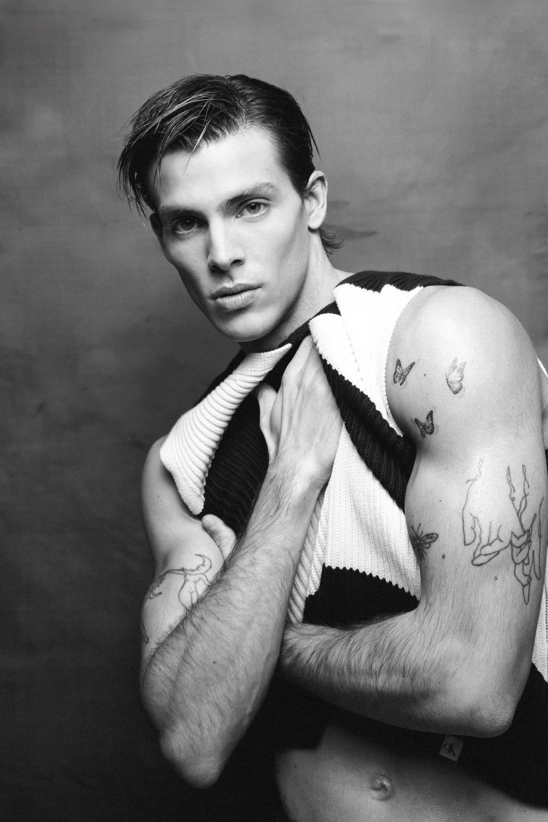 Man with tattoos, holding a black and white striped garment, looking at the camera with a serious expression