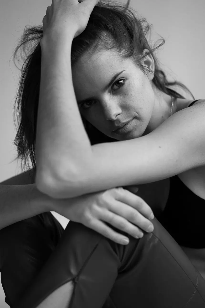 Woman with dark hair, looking intently at the camera, arms crossed, seated