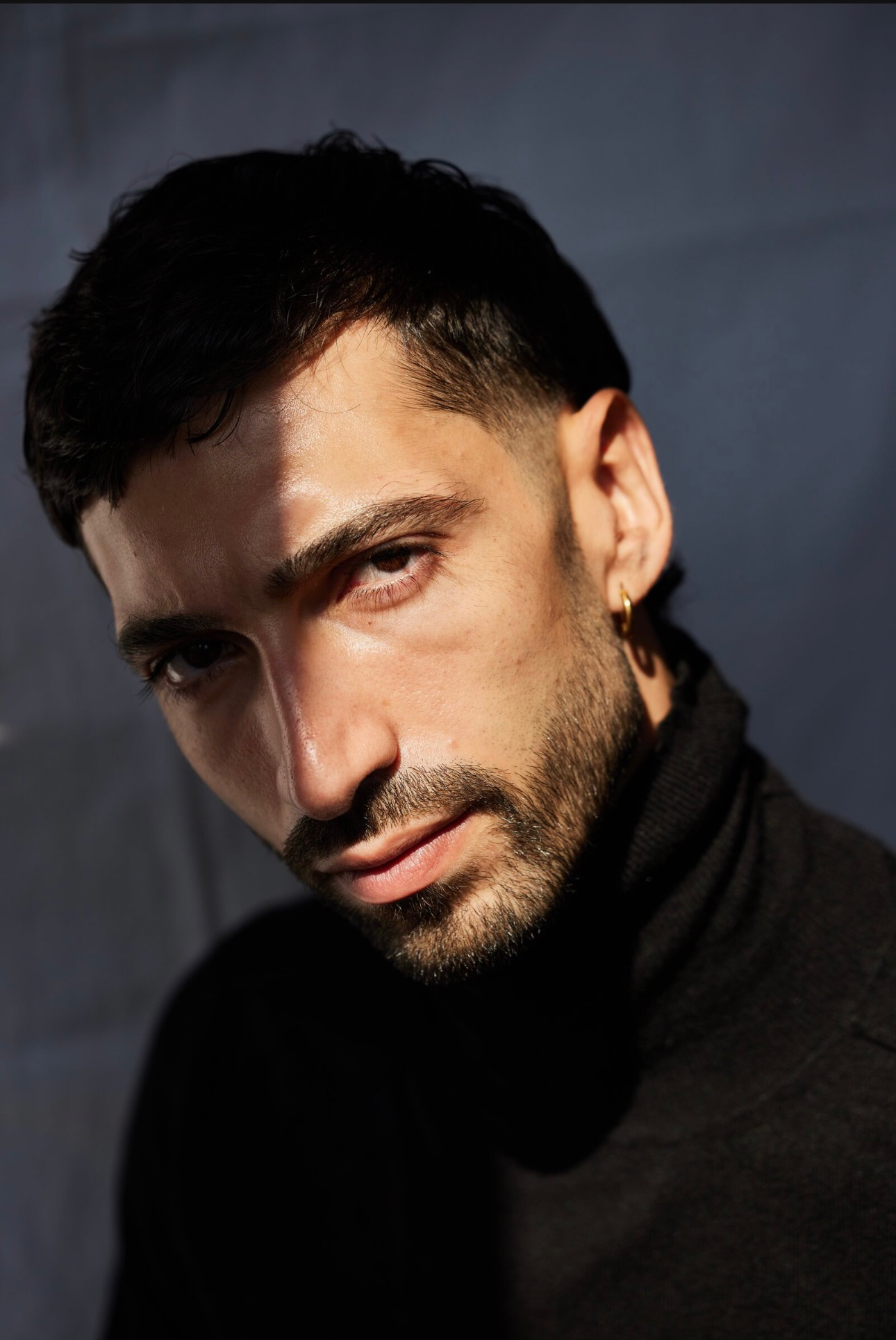 Fashion model in a dynamic pose, wearing a tailored black blazer over a white shirt and dark trousers, standing against a minimalist studio backdrop during a professional photoshoot