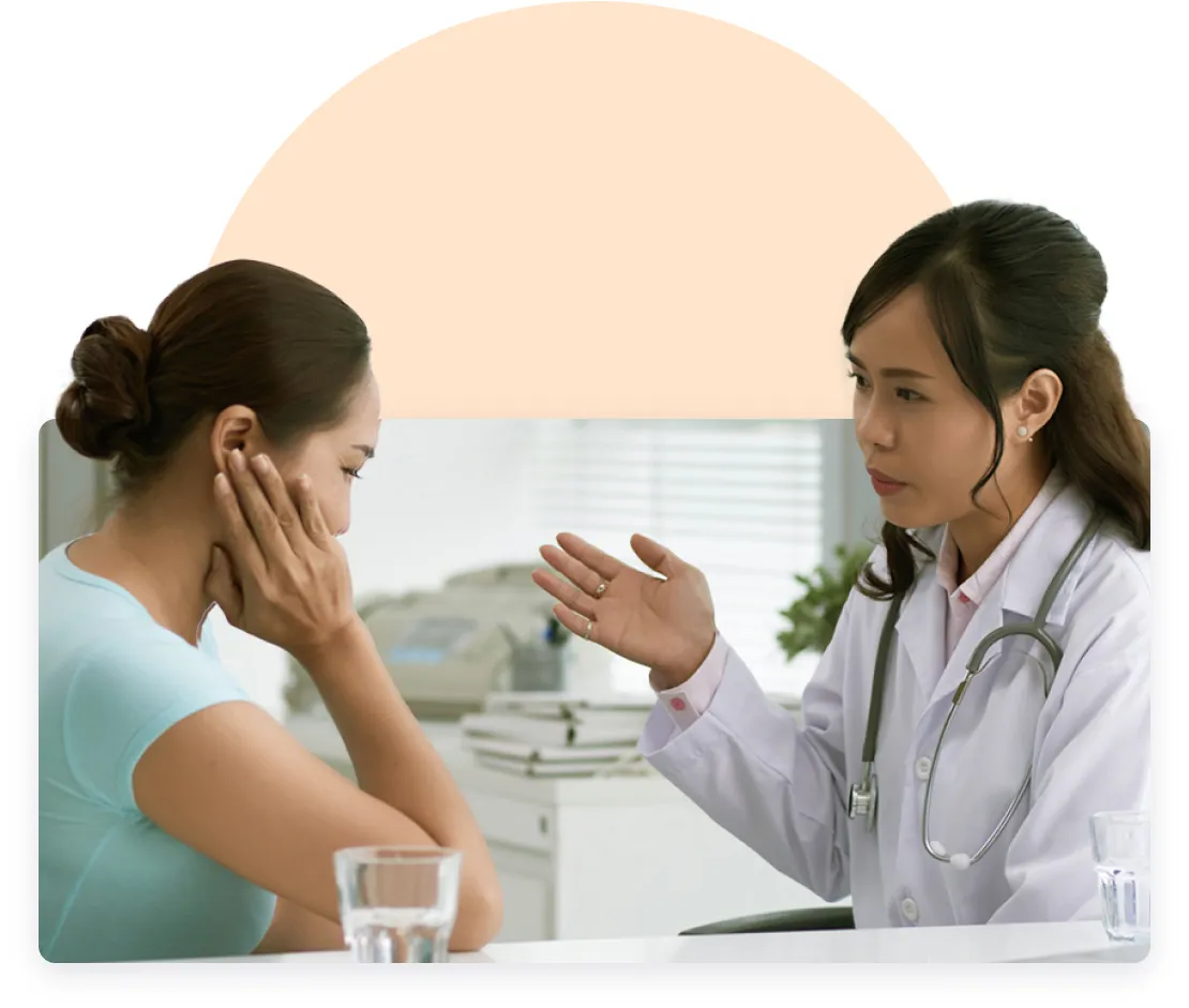 A patient holding her cheek in discomfort, speaking with a concerned doctor in a medical office.