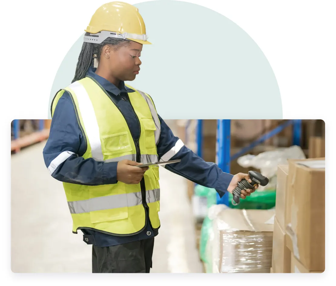 The image depicts a worker wearing safety gear, including a yellow hard hat and a high-visibility vest, in a warehouse setting. The individual is holding a clipboard in one hand and a barcode scanner in the other, seemingly checking inventory or scanning items. The background suggests a storage or warehouse environment with shelved goods.