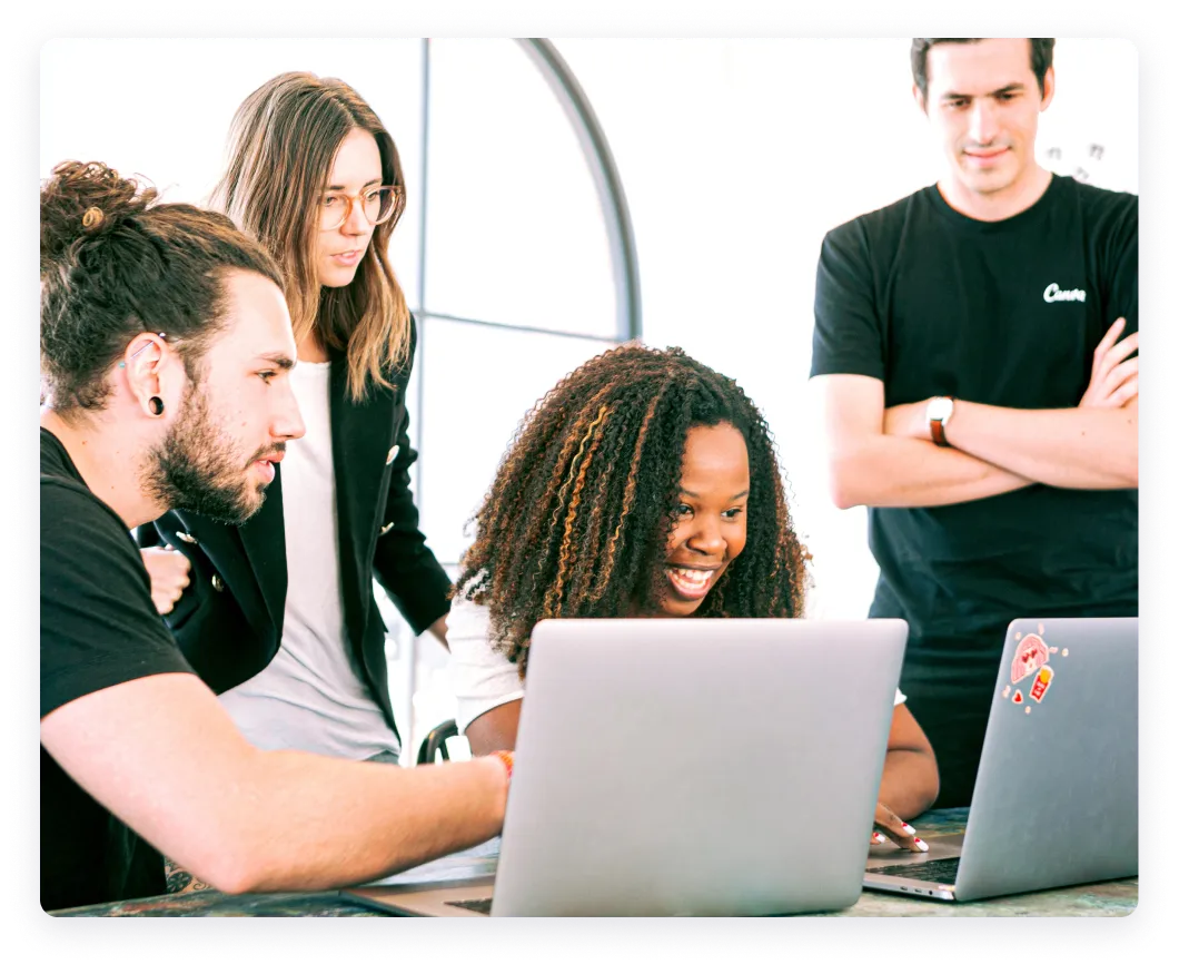 Team members collaborating around laptops in a bright workspace.