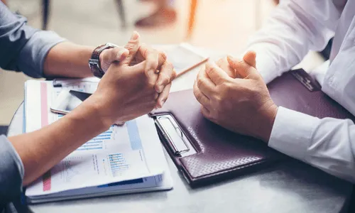 Two employees crossing their hands across a table. They are negotiating something. 