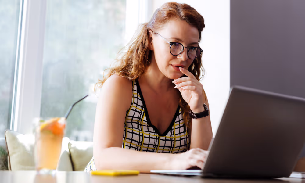 Woman working on her laptop. There is a drink on her desk, presumably a cup of lemonade.