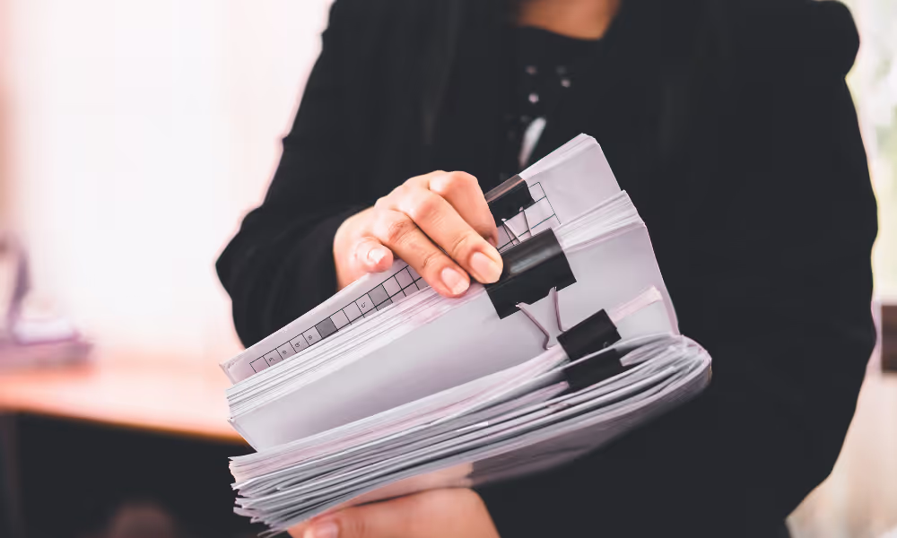 Person holding a stack of documents. The face is not shown in this image.